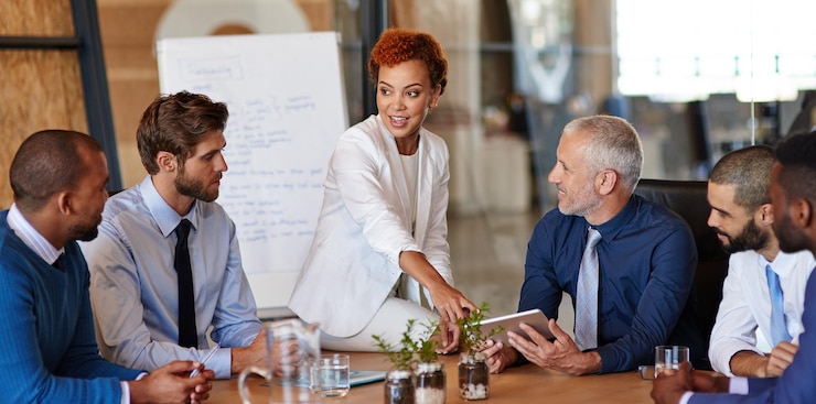 A team meeting around a table with a laptop and plants