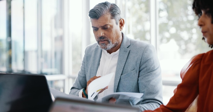 A man in a grey jacket reading at his laptop in an open office